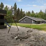 Ein Ferienhaus mit Spielplatz, Sandkasten und Grünfläche im Wald.