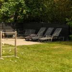 Garten mit Liegestühlen und Spielgerät vor dunklem Holzzaun.