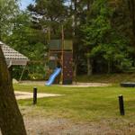 Hinterhof mit Spielplatz, Rutsche und Kletterwand. Grasfläche und Wald im Hintergrund.