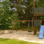 Kinderbereich mit Sandkasten, Rutsche und Kletterwand im Wald.