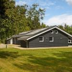 Ein dunkelgraues Haus mit weißen Fensterrahmen und einer grünen Wiese im Vordergrund.