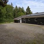Schwarzes Holzhaus mit Solaranlage und Terrasse im Wald. Kiesfläche vor dem Gebäude.