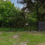 Gartenbereich mit Zaun, Grasfläche und Bäumen im Hintergrund.