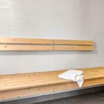 Holzbank mit Rückenlehne in Sauna mit weißer Wand und grauem Boden