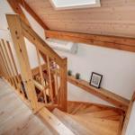 Holzgetreppe mit Geländer führt zur oberen Etage. Decke und Wände sind weiß.