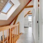 Haus mit Holzdecke, Dachfenster und Holzgeländer. Blick in einen Flur mit weißen Wänden.