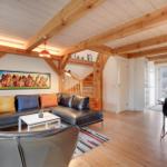 Wohn- und Essbereich mit Holzdecke, Sofa und Tisch. Treppenhaus im Hintergrund.
