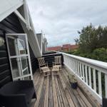 Terrasse mit Holzdielen, zwei Stühlen und weißer Brüstung. Blick auf Bäume und Häuser.