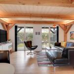 Wohnzimmer mit Holzbalkendecke, Sofa, Fernseher und Glastüren zum Garten.