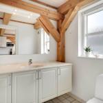 Badezimmer mit Waschbecken, Spiegel und Fenster. Holzbalken an der Decke.