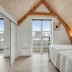 Schlafzimmer mit Dachschrägen, Holzboden und Fenster zum Balkon.