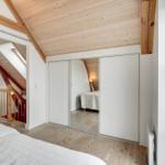 Schlafzimmer mit Holzboden, Spiegelschrank und Dachschrägen. Blick auf Treppenhaus.