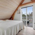 Schlafzimmer mit Balkon und Holzwand. Bett mit weißer Bettwäsche.