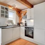 Küche mit weißen Schränken, schwarzer Arbeitsplatte und Holzbalken an der Decke.