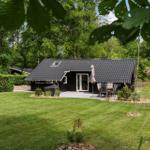 Ein schwarzes Ferienhaus mit Terrasse und Garten inmitten von Bäumen.