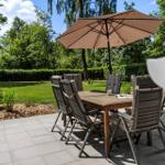Terrasse mit Tisch, Stühlen und Sonnenschirm. Grünfläche und Bäume im Hintergrund.