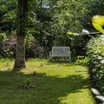 Ein weißer Sitzplatz im grünen Garten unter Bäumen.