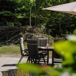 Terrasse mit Tisch, Stühlen und Sonnenschirm im Grünen.