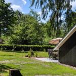 Schwarzes Holzhaus mit Garten, Terrasse und Flagge. Umgeben von Bäumen und Gras.