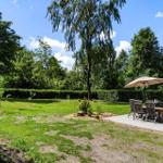 Hinterhof mit Grillplatz, Sitzgruppe unter Sonnenschutz und Flagge. Grünfläche und Bäume umgeben den Bereich.