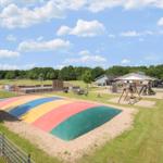 Großer Spielplatz mit buntem Rutsch- und Kletterbereich, Sandfläche und Holzspielgeräten.