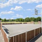 Basketballplatz mit Holzumzäunung und Korb unter blauem Himmel.