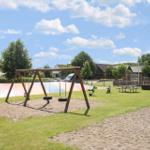 Spielplatz mit Schaukel, Sandkasten und Picknicktisch im Freien.