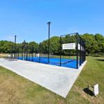 Blauer Futsalplatz mit Zaun und Beleuchtung im Grünbereich.