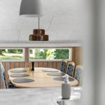 Rundes Esszimmer mit Holztisch, Stühlen und Fenstern. Hängelampe über dem Tisch.
