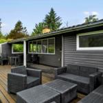 Terrasse mit Sitzgruppe und Tisch. Haus mit dunkler Fassade und Fenstern.
