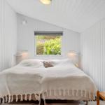 Ein Schlafzimmer mit weißem Bett, Wandpaneelen und Fenster zur Außenseite.