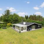Schwarzes Haus mit Glasveranda, Garten und Liegestühlen. Umgeben von Bäumen und Grün.