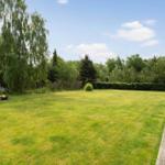 Großer Garten mit Rasenfläche, Holzterrasse und Feuerkorb. Umgeben von Bäumen und Sträuchern.