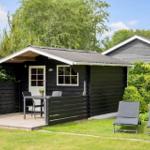 Schwarze Hütte mit Terrasse, Tisch, Stühlen und Liegestühlen im Garten.