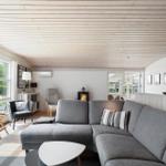 Wohnzimmer mit grauem Sofa, Kamin und großen Fenstern zur grünen Außenansicht.