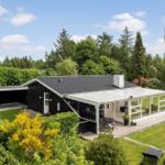 Modernes Haus mit Terrasse und Garten. Umgeben von Bäumen und grünem Rasen.