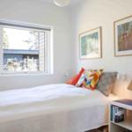Bedroom with bed, window, and wall art. Nightstand with lamp and books.