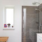 Bathroom with shower, window, and sink. Wooden stool and decor on windowsill.