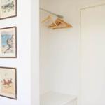 Closet with wooden rod and hooks. Wall with three framed pictures. View into kitchen area.
