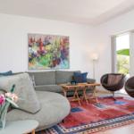 Living room with sofa, two chairs, rug, and wall art. Entrance to terrace with umbrella.