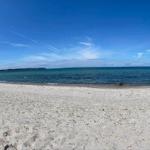 Beach with white sand, blue sea, and two people with a green kayak.