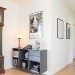 Hallway with antique grandfather clock, framed photos, and gray sideboard with books and games.