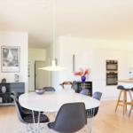Dining area with round table and chairs, kitchen with countertop and bar stools.
