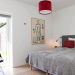 Bedroom with bed, red pendant lamp, and artwork on wall. Door leads outside.