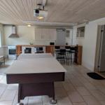 Room with ping pong table, kitchen, and bar stools.