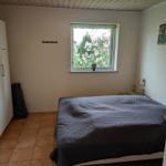 Bedroom with bed, wardrobe, and window with view of flowers.