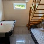Room with air hockey table, sofa bed, and wooden staircase. Window with view of green area.