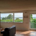 Living area with water and green view, black sofa, terrace door and windows.