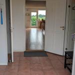 Entrance area with door and tiled floor. Corridor leads to living area with table and chairs.