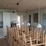Large dining area with wooden chairs and pendant lights. Kitchen in the background.